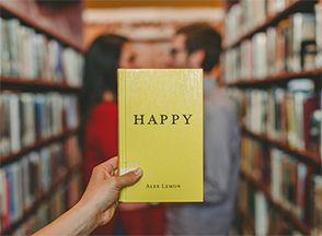 Couple in the library and a hand holding the book "Happy"