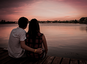 A couple with their arms around each other looking at sunset.