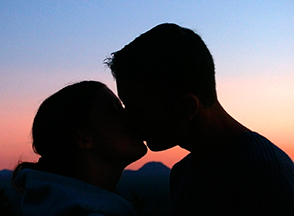 Man in woman kissing in sunset.