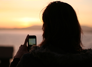 A woman on her cell phone with her back towards us  at sunset.